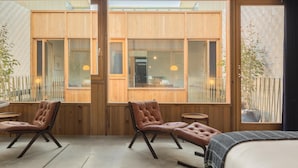 Una habitación moderna con una cama grande, dos sillones de cuero, una mesita y ventanas amplias con vistas al exterior.