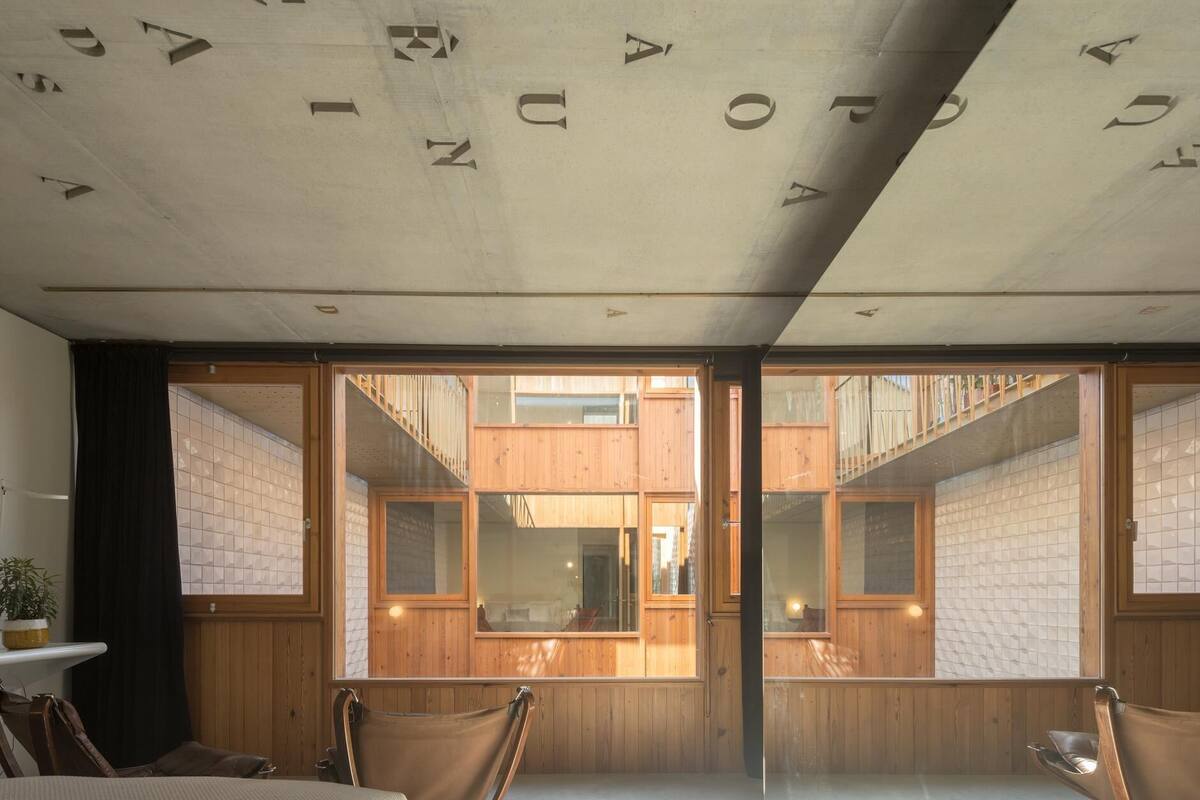 Habitación de hotel moderna con una cama grande, dos sillas de madera y vistas al exterior a través de puertas de cristal.