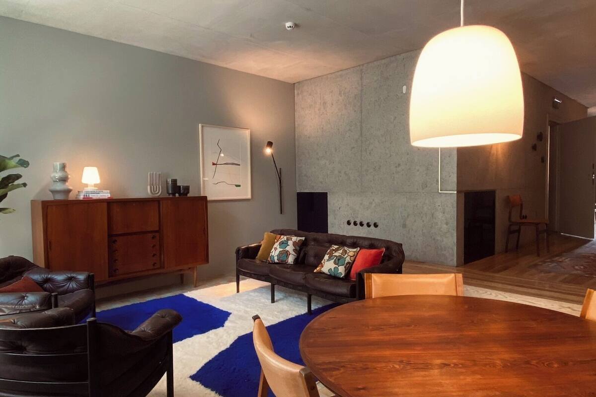 Una sala moderna con una mesa de comedor de madera, sofás de cuero y un tapete azul.