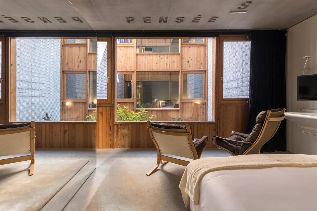 Una habitación moderna con una cama grande, dos sillones y vistas a la ciudad a través de amplios ventanales.