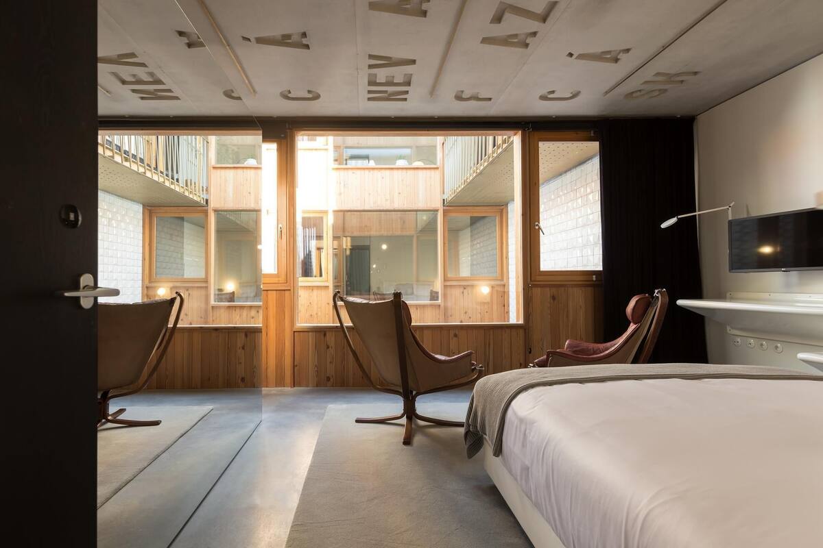 Una habitación de hotel moderna con una cama grande, dos sillones, un televisor y un techo con letras grandes.