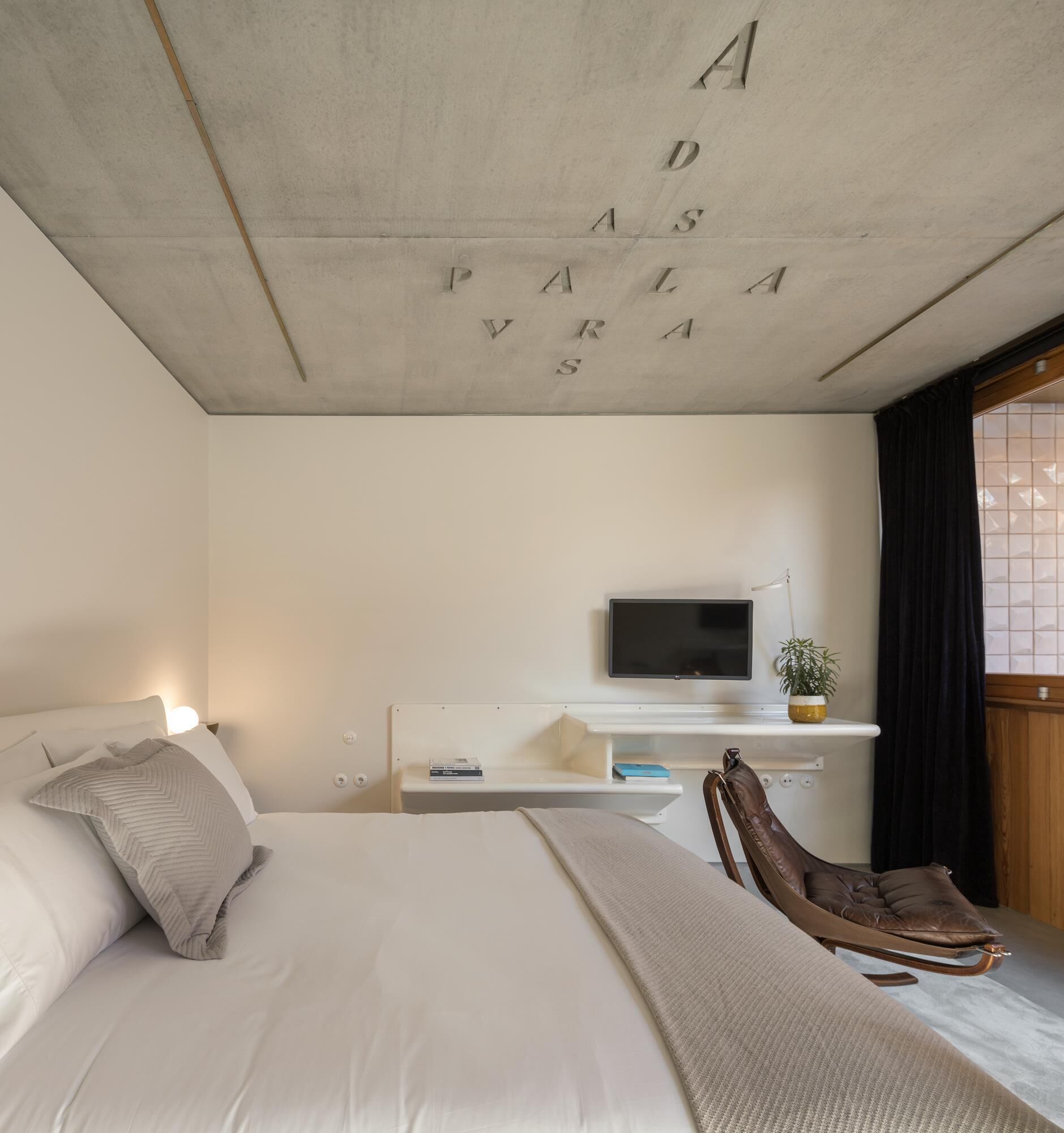 Une chambre à coucher avec un lit, un bureau avec une télévision, une chaise et un plafond orné de lettres.