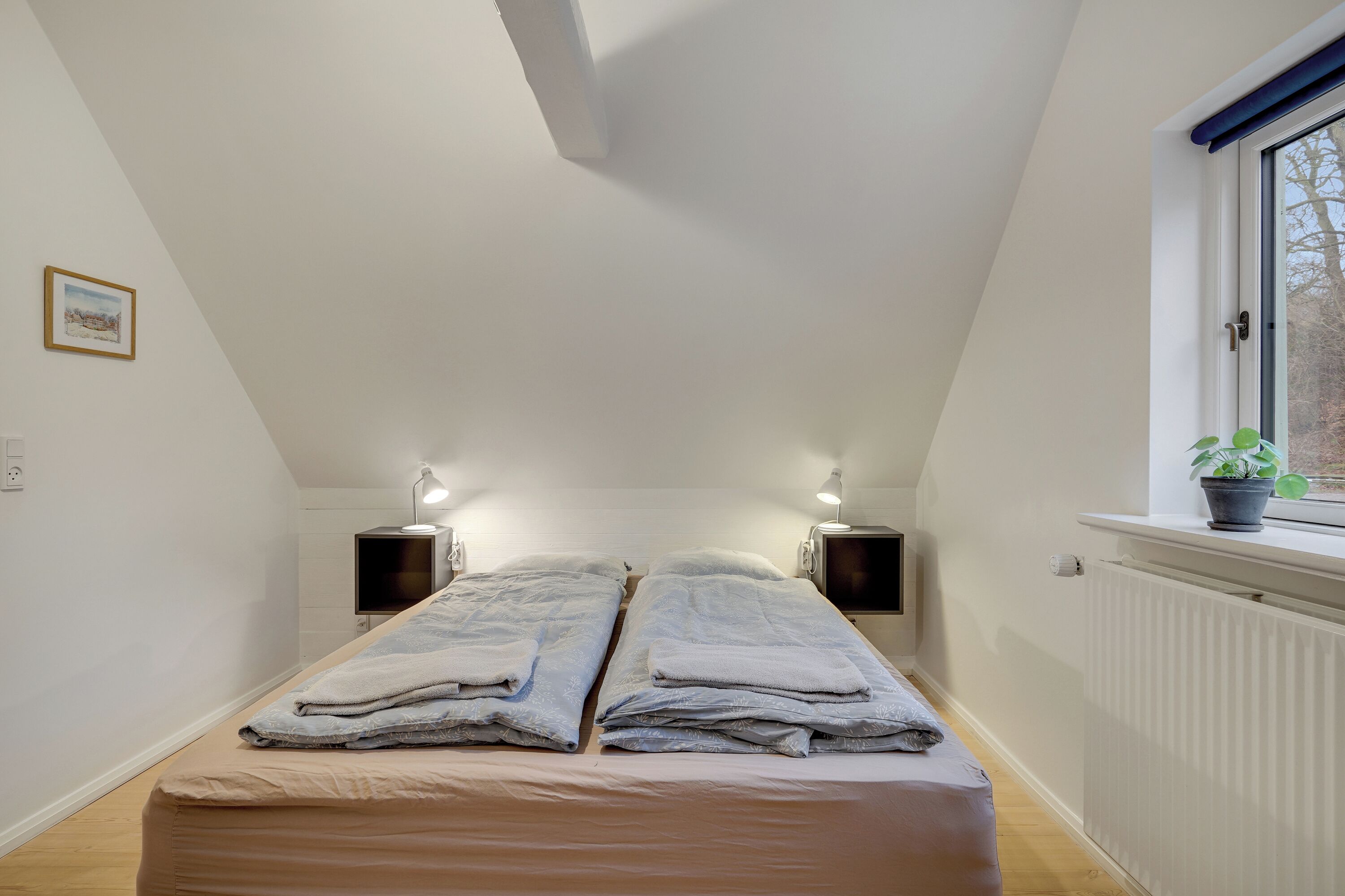 Une chambre à coucher avec un lit, des lampes de chevet, une fenêtre donnant sur un beau paysage et un radiateur.