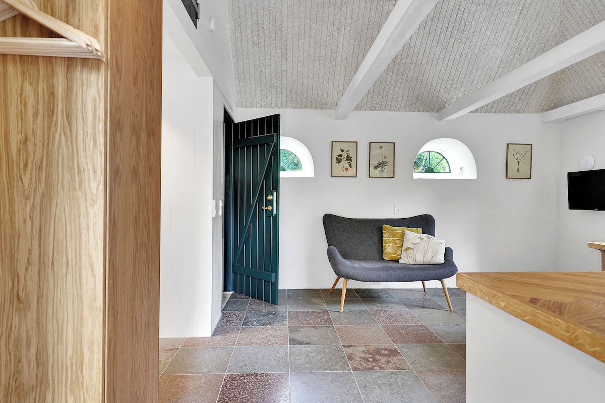 A modern interior with a wooden door, a dark green door, a grey sofa, and a wooden counter.