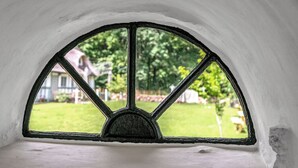 A room with a semi-circular window with a black frame, a white wall, and a view of a green lawn and a house in the background.