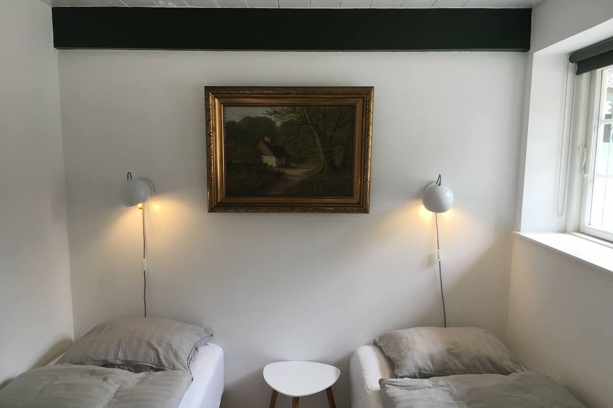 A room with two beds, a small table, and a painting on the wall.