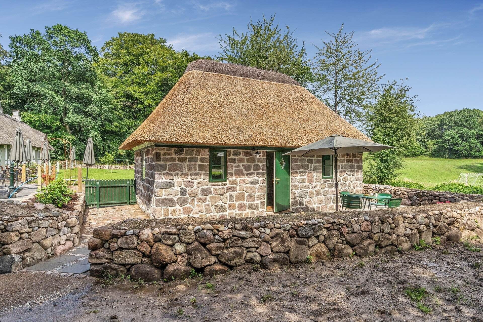 A stone cottage with a thatched roof, a green door, and a stone wall in front.