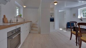 A modern kitchen with white cabinetry, a wooden countertop, and a built-in oven. There is a staircase leading to a dining area with a blue chair and a wooden dining table.