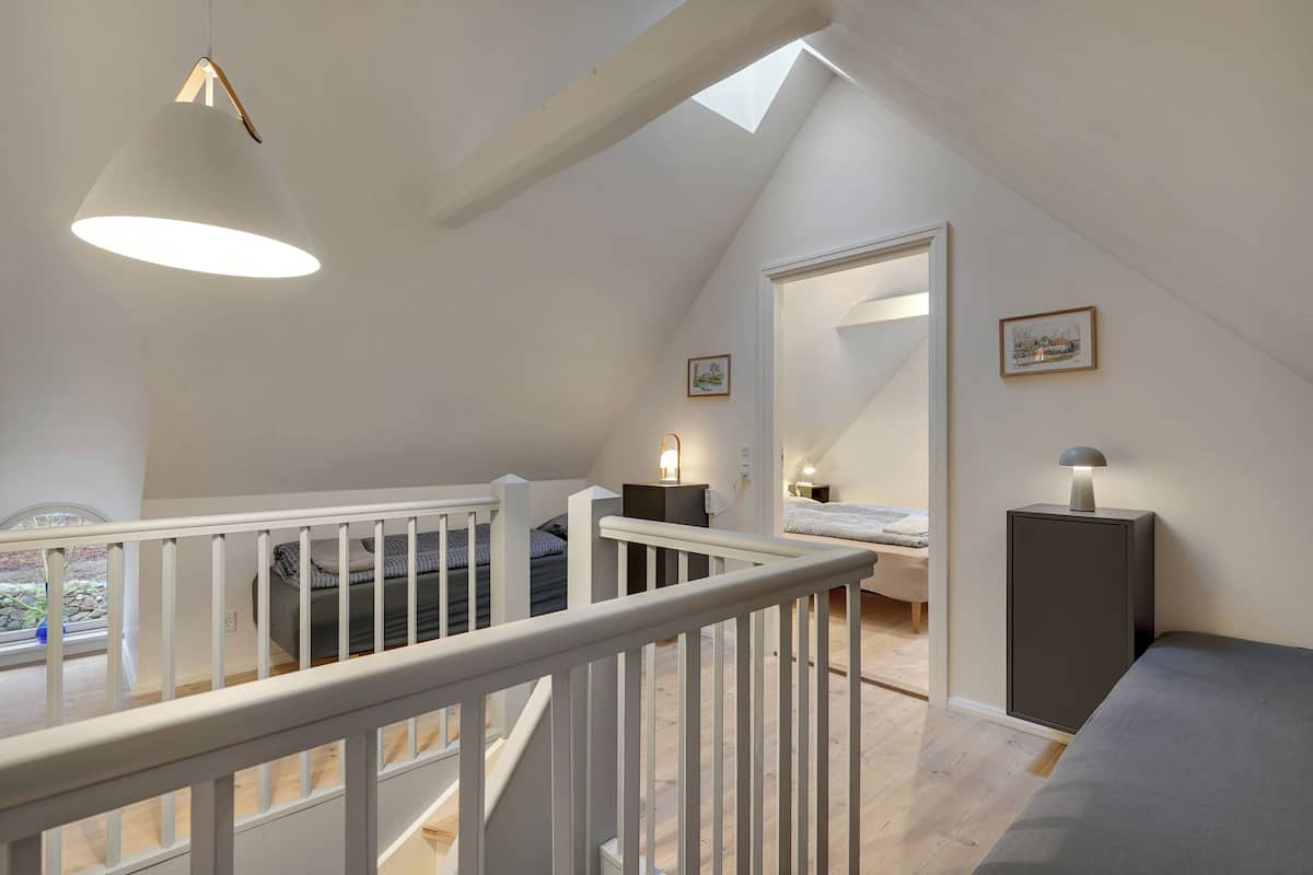 A spacious loft bedroom with a high ceiling, a skylight, a large bed, a bedside table, and a nightstand.