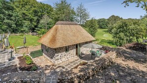 A stone cottage with a thatched roof, surrounded by a stone wall and a paved patio.