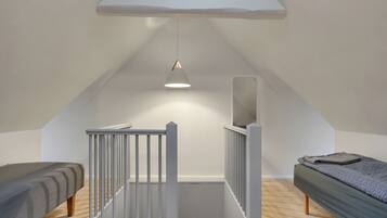 A small, modern room with a sloped ceiling, a single bed, a small desk, and a hanging light fixture.