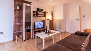A living room with a TV, white coffee table, brown sofa, wooden shelving, and a radiator. - Vacation apartment Leer-Stadtmitte 15131 - Holiday apartment Leer-Stadtmitte (Leer (Ostfriesland))