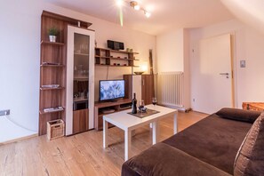A living room with a TV, white coffee table, brown sofa, wooden shelving, and a radiator.