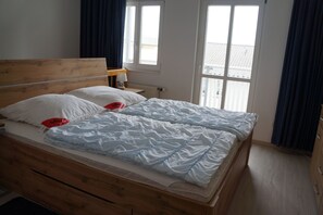 Un letto matrimoniale con testiera in legno, un comodino con una lampada e vista su un balcone attraverso una finestra.