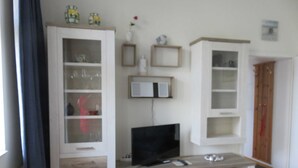 A living room with a TV, cabinets, and a small table. - 2-room apartment - House Quisisana - Apartment 45496 (Göhren)