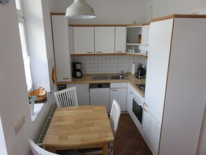 Una cucina compatta con mobili bianchi, un tavolo da pranzo in legno e una sedia bianca.