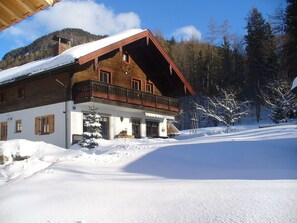 Eine Holzhütte mit Balkon, umgeben von verschneitem Gelände und Bäumen.