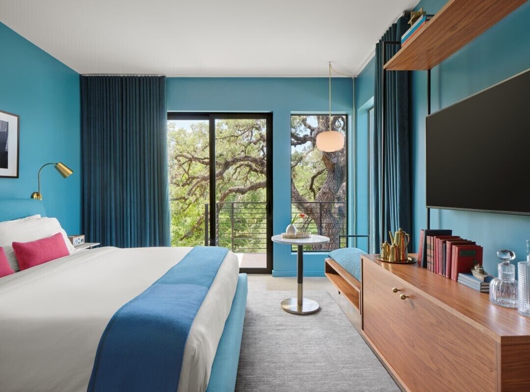 Une chambre d’hôtel moderne, dotée d’un grand lit, d’un bureau, d’une chaise et offrant une vue sur les arbres par la fenêtre.