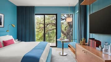 Une chambre d’hôtel moderne, dotée d’un grand lit, d’un bureau, d’une chaise et offrant une vue sur les arbres par la fenêtre.