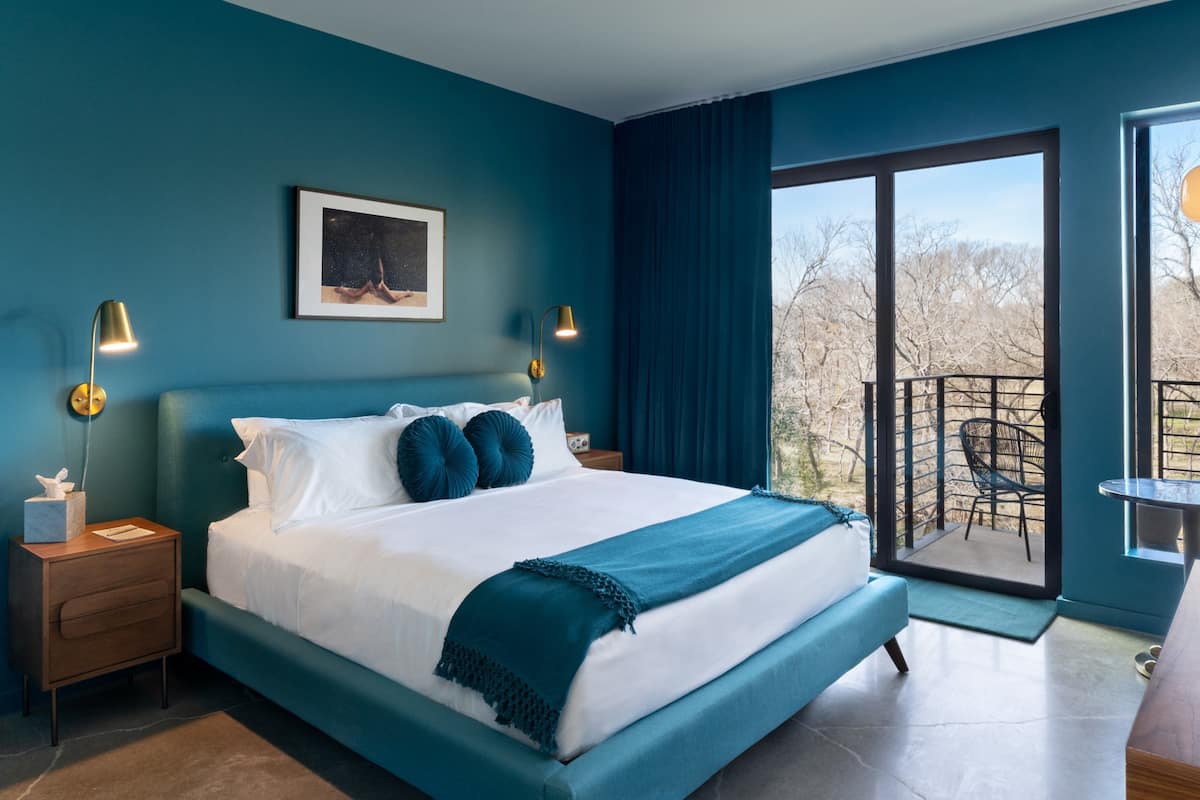 Ein modernes Schlafzimmer mit einem großen Bett, zwei Nachttischlampen, einem gerahmten Bild und einem Balkon mit Blick.