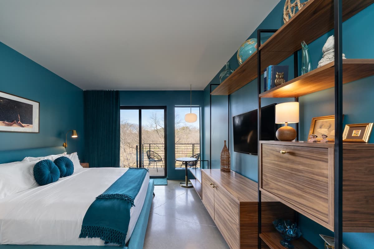 Ein modernes Schlafzimmer mit einem großen Bett, einem Schreibtisch und Blick durch eine Schiebetür auf einen Balkon.