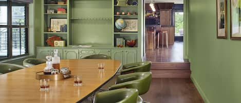 A conference room with a long table, green chairs, and a bookshelf with various items.
