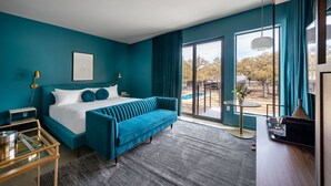 A modern hotel room with a large bed, a blue sofa, a desk, and a view of the outdoors. - The Ruby Hotel (Round Rock)