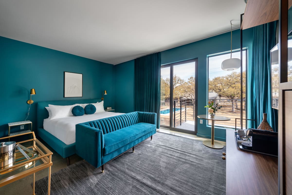 Ein modernes Hotelzimmer mit einem großen Bett, einem blauen Sofa, einem Schreibtisch und Blick ins Freie.