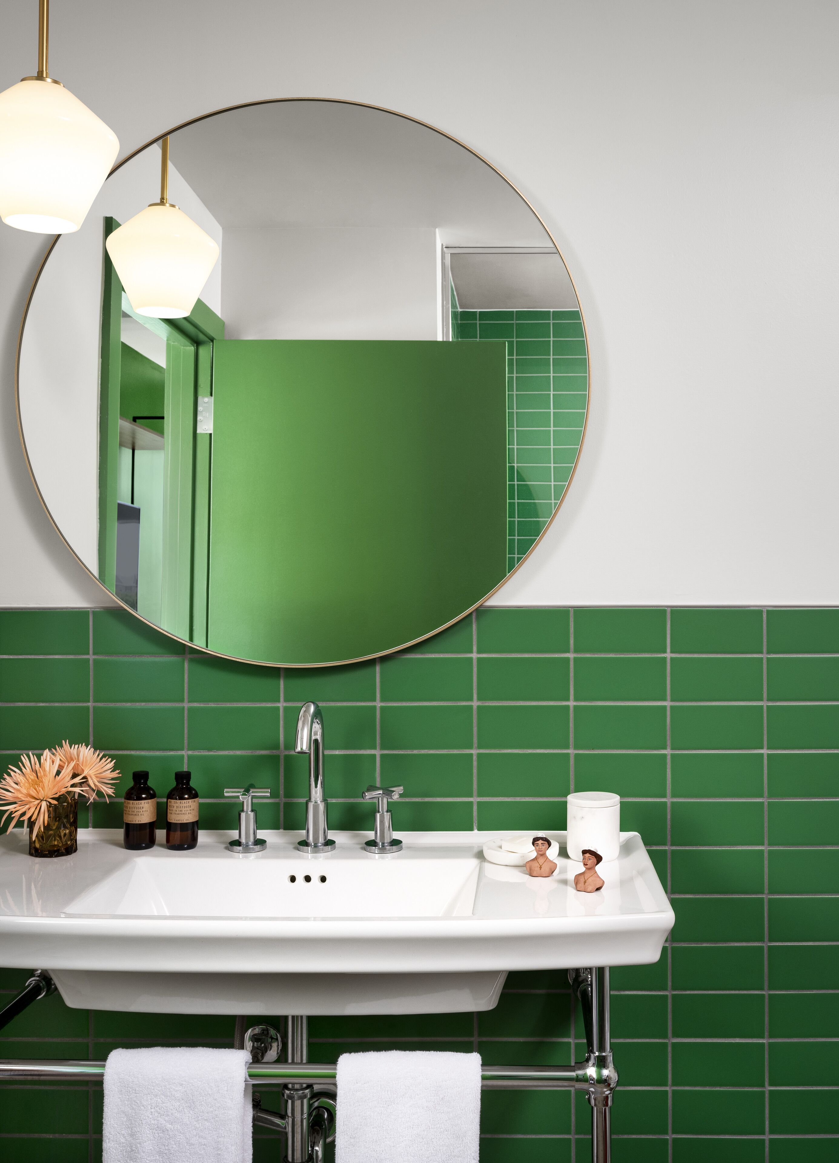 A bathroom with a white sink, green tiles, a round mirror, and a towel rack.