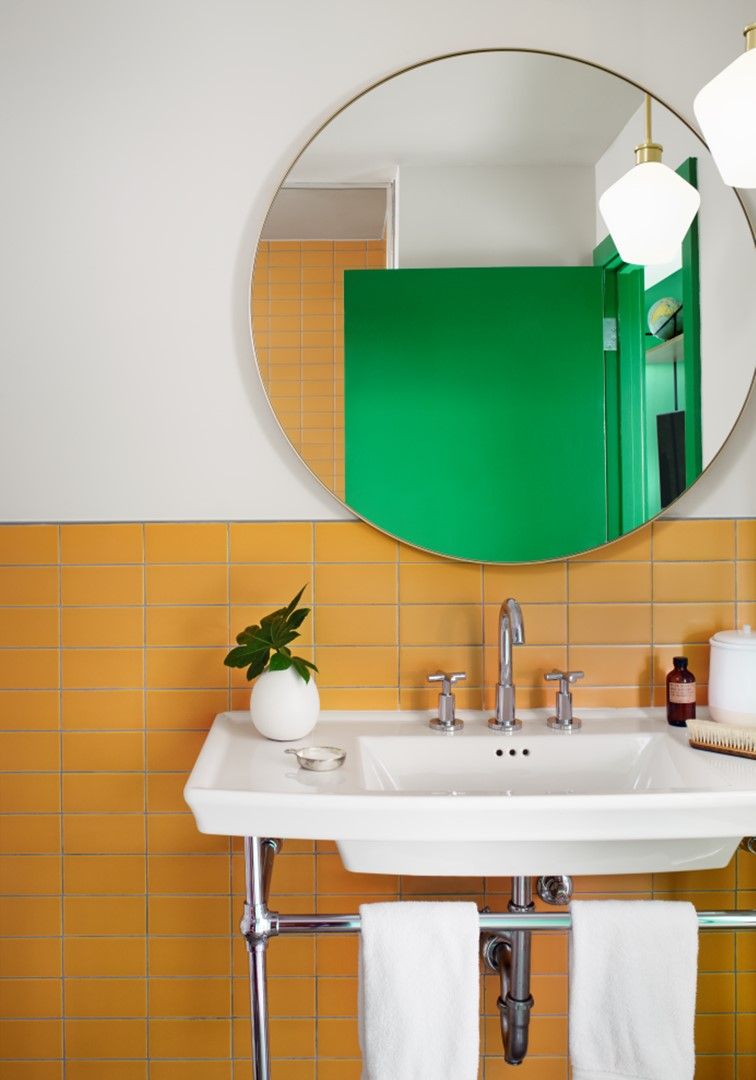 A bathroom with a white sink, green mirror, and orange tiled wall.