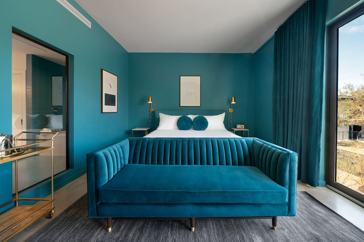 Ein schlafgemütliches Zimmer in Türkis mit einer samtenen Couch, einer Glastruhe und Blick ins Freie.