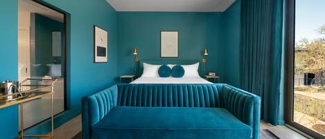 A teal-themed bedroom with a tufted sofa, a glass cabinet, and a view of the outdoors.