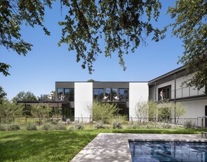 A modern two-story house with a swimming pool, surrounded by a well-maintained garden and a clear blue sky.