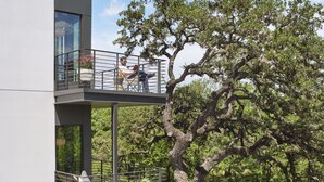 A modern two-story building with a balcony overlooking a river and a large tree. - The Ruby Hotel (Round Rock)