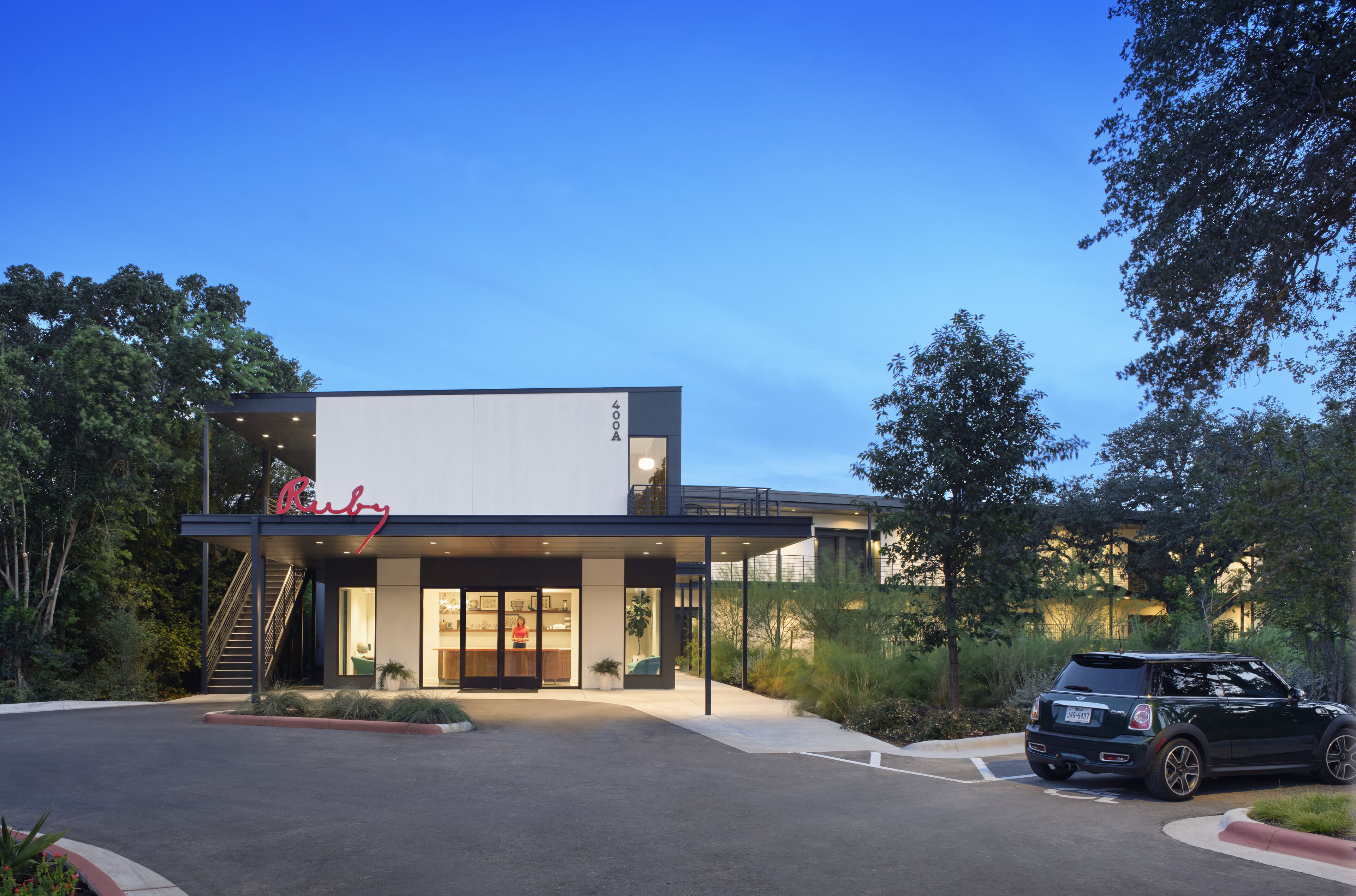 A modern building with a prominent sign, a covered entrance, and a parking area with a car.