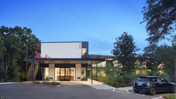 A modern building with a prominent sign, a covered entrance, and a parking area with a car.