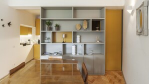 A modern dining area with a wooden table and chairs, a built-in shelf unit with decorative items, and a yellow accent wall. - CdC Apartments By Casa do Conto (Porto)