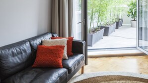 A modern living room with a leather sofa, two patterned cushions, and a view of a garden through a glass door. - CdC Apartments By Casa do Conto (Porto)