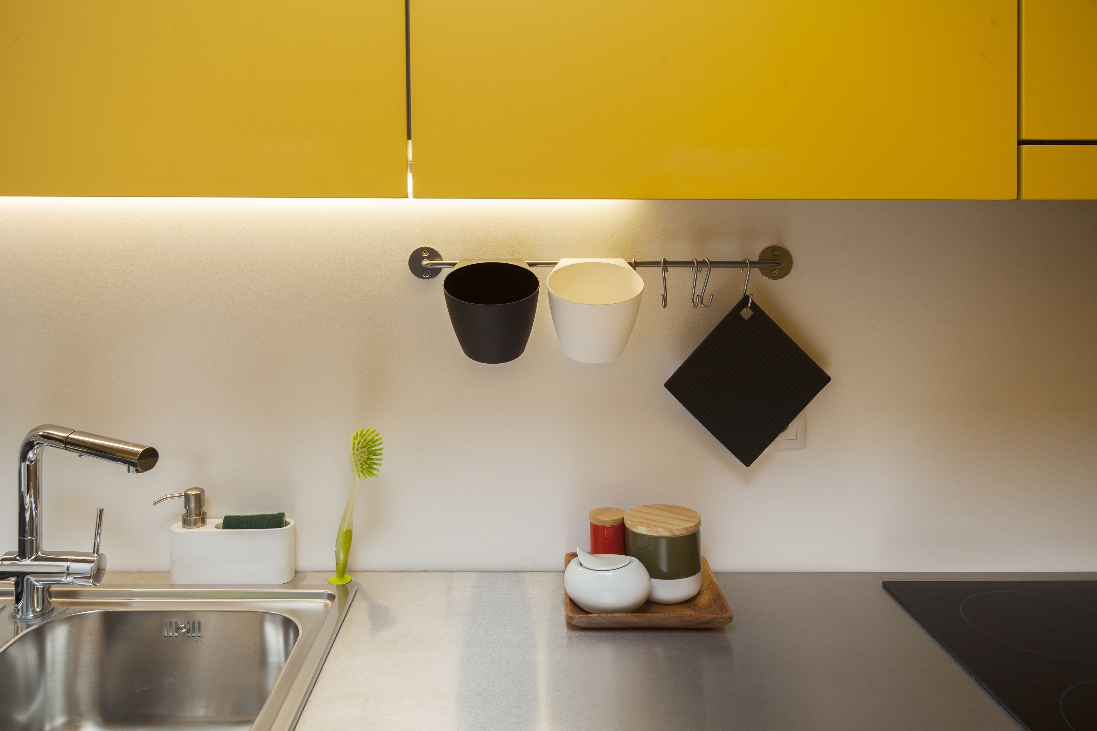 A kitchen with a stainless steel sink, a white countertop, and a wooden cutting board with a white teapot and two wooden containers.