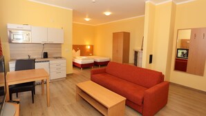 Un espacio habitable compacto con kitchenette, un sofá, una mesa de comedor y una cama.