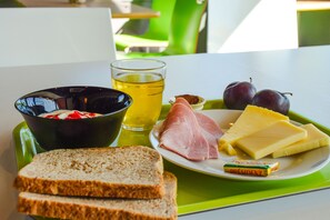 A meal tray with bread, ham, cheese, plums, a bowl of fruit, and a glass of juice.