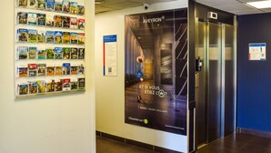 A hallway with a travel poster, a book display, and an elevator. - Ibis Budget Rodez (Rodez)