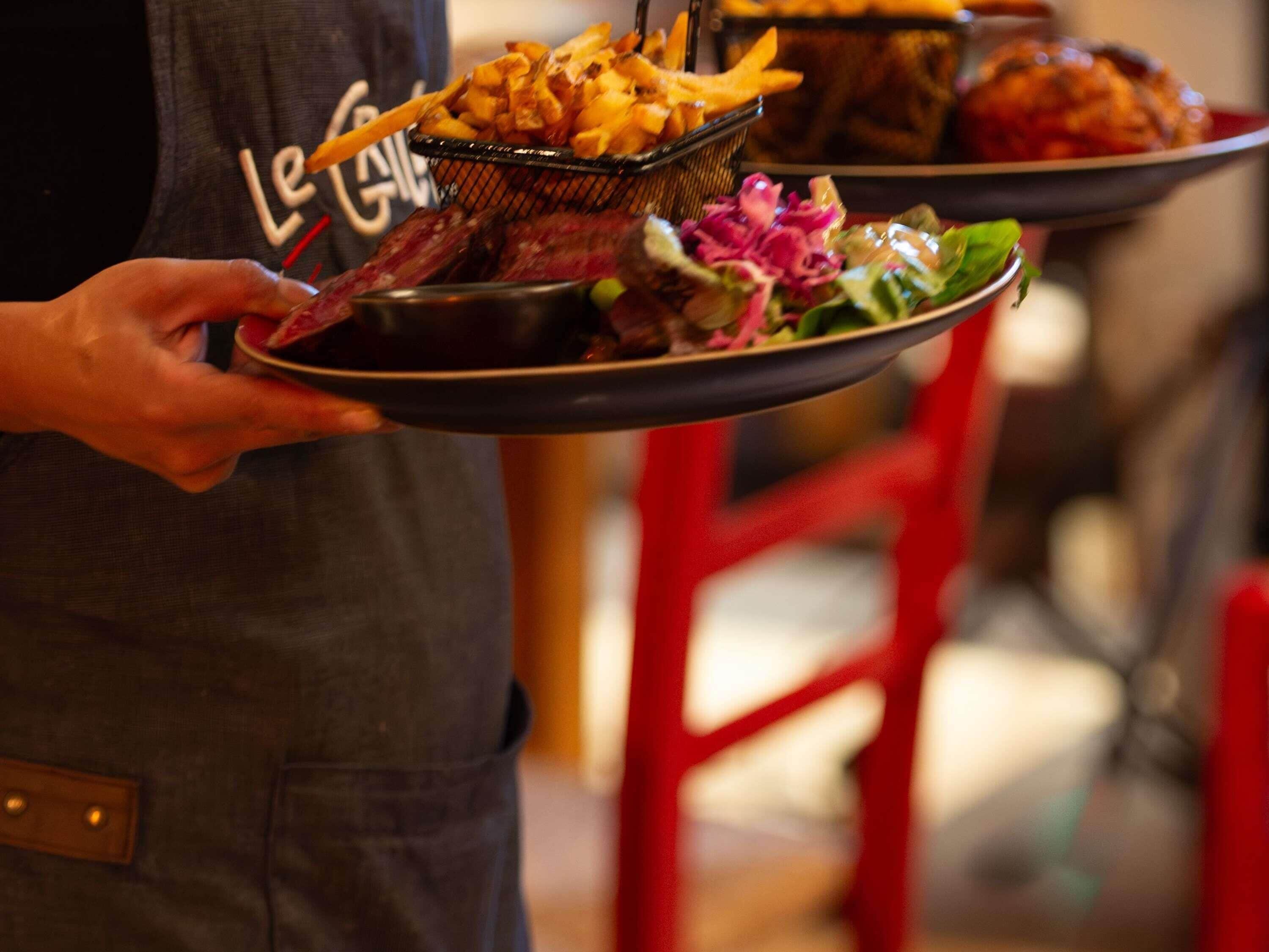 Una persona sosteniendo un plato con papas fritas, carne y ensalada.