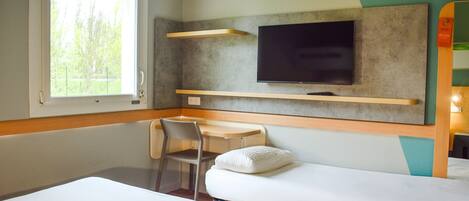 Una habitación con dos camas, un escritorio, una silla, un televisor y una ventana.