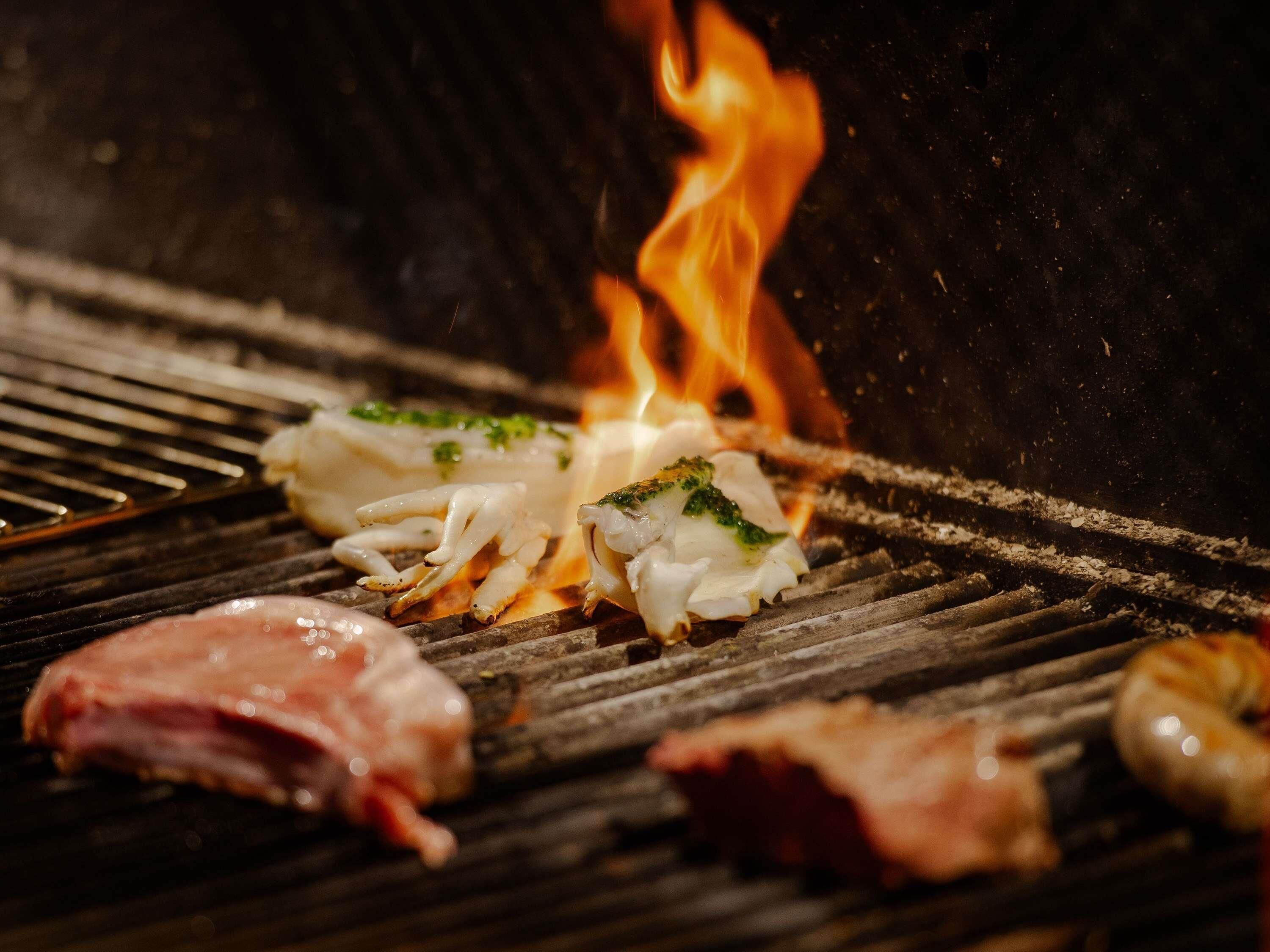 Una parrilla con diferentes carnes y mariscos cocinándose a fuego abierto.