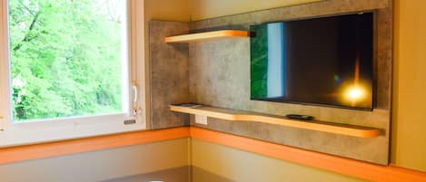 Una habitación con cama, ventana con vistas a vegetación, televisor de pantalla plana en la pared y una pequeña mesa.