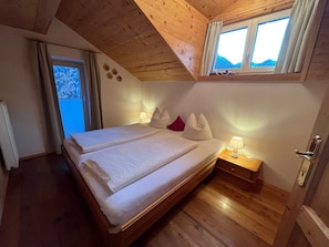 A bedroom with a wooden ceiling, a bed with white bedding, a nightstand with a lamp, and a window with curtains.