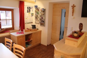 Ein Zimmer mit Holzmöbeln, einem Korkbrett mit Papieren, einer Holztür und einem Kruzifix an der Wand.