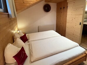 Un dormitorio con techo de madera, una cama blanca con almohadas rojas, un radiador blanco y una pared de madera.