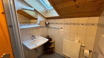 Ein Badezimmer mit Oberlicht, Waschbecken, Toilette und Duschbereich.